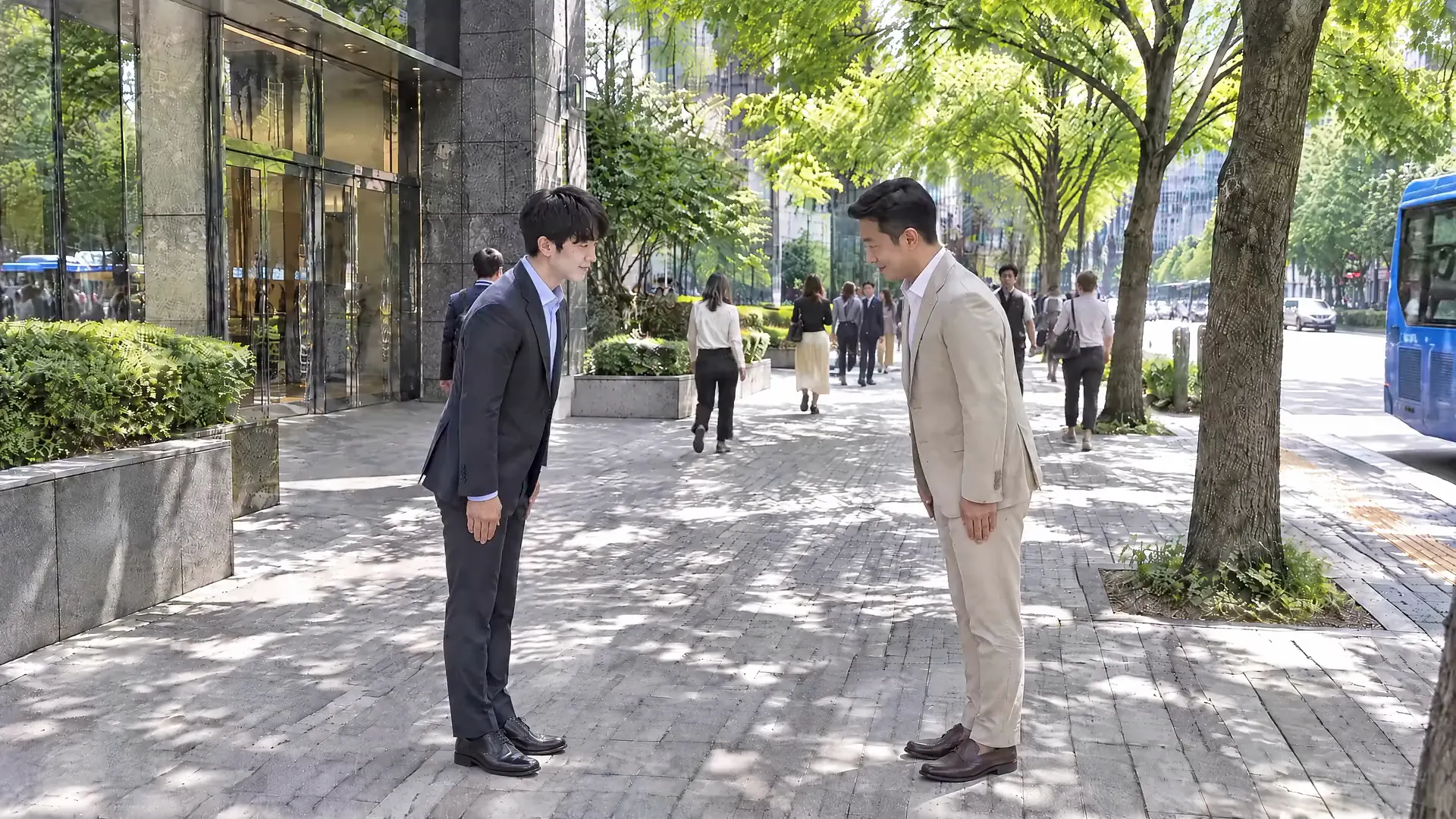 브랜드 영상 장면: 가로수 길에서 정장 차림의 두 사람이 목례로 인사한 뒤 함께 걷는 모습